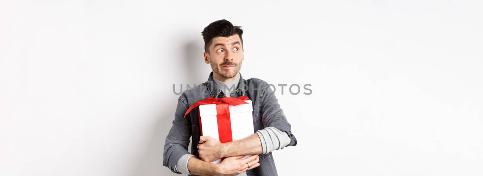 Excited man hugging romantic gift for girlfriend, waiting for valentines date with lover, looking at empty space logo with happy face, standing on white background.
