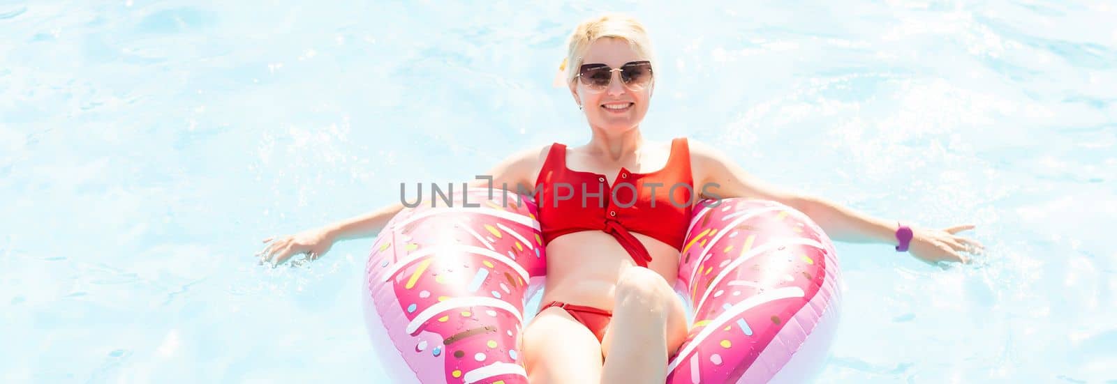 Woman relaxing on donut lilo in the pool at private villa. Inflatable ring and mattress. Summer holiday idyllic. High view from above by Andelov13
