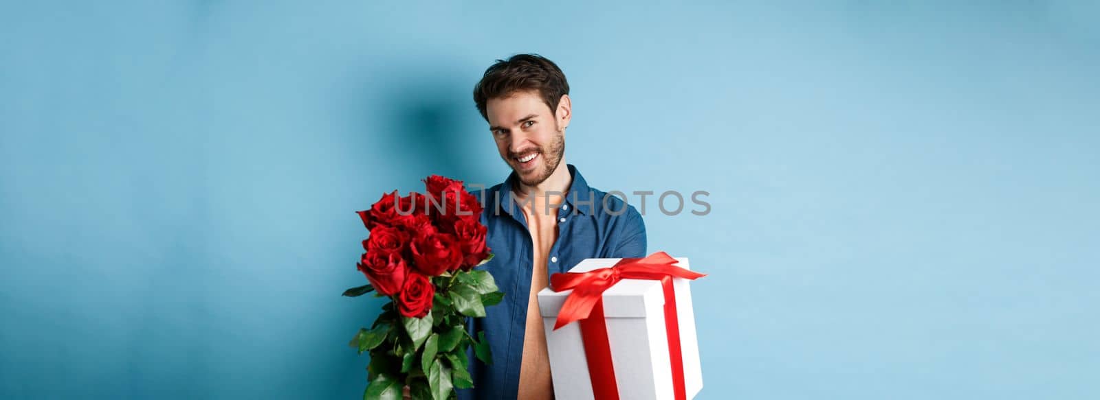 Love and Valentines day concept. Romantic smiling man giving you gift box and bouquet of flowers on date, standing over blue background by Benzoix