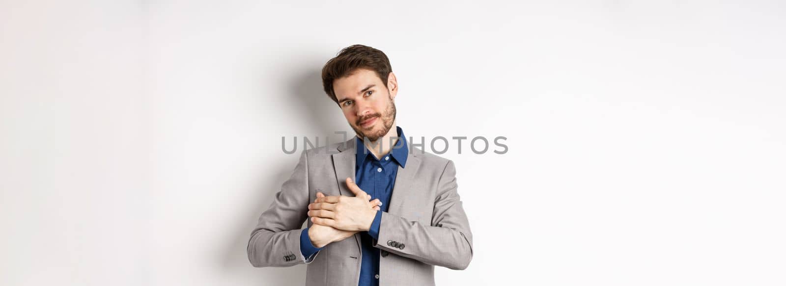 Romantic handsome guy with beard holding hands on heart and smiling, thanking you, feeling nostalgic, having tender memories in heart, white background.