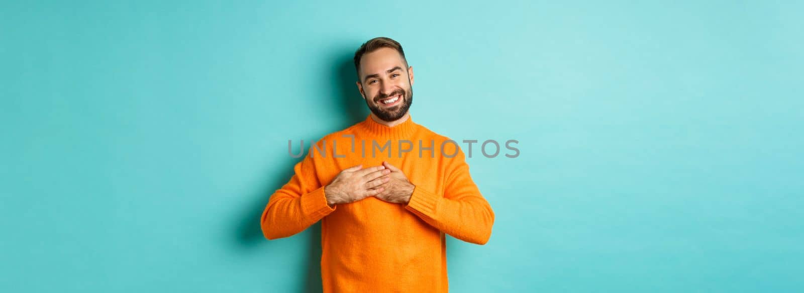 Grateful man smiling, holding hands on heart, thank you gesture, feeling touched with gift, standing over turquoise background by Benzoix