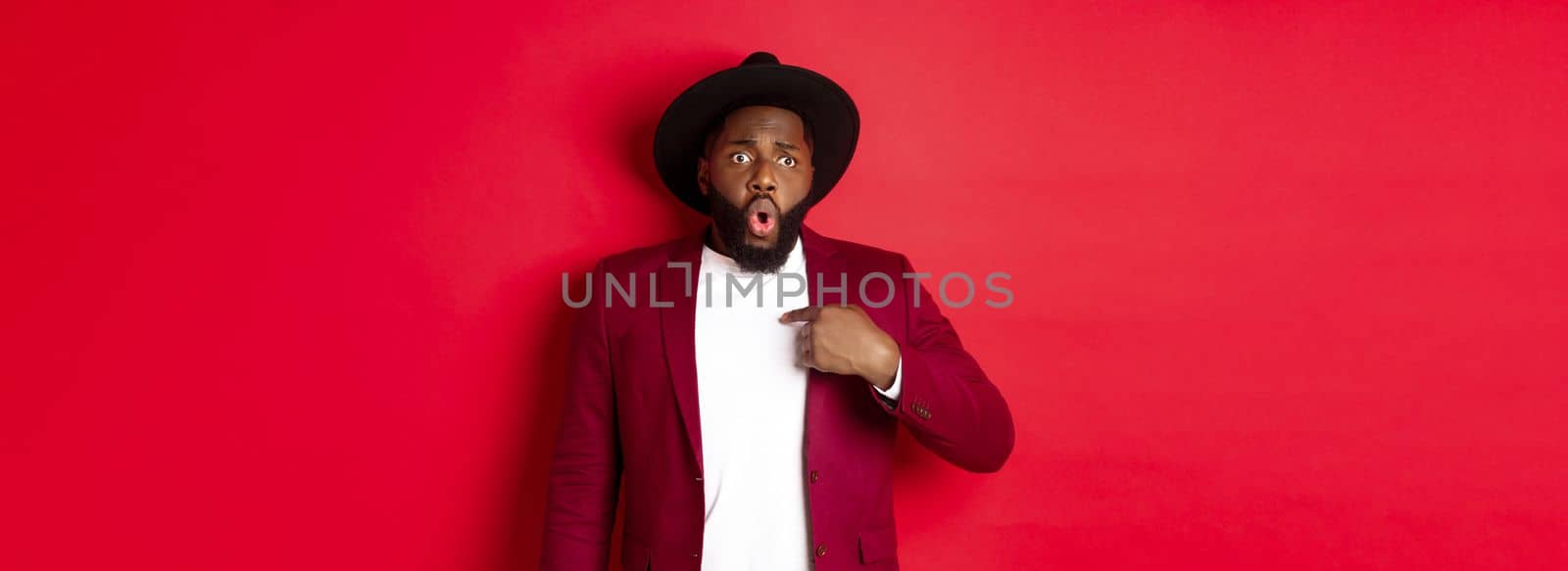 Christmas shopping and people concept. Worried african american man pointing at himself, being accused, standing nervous against red background.