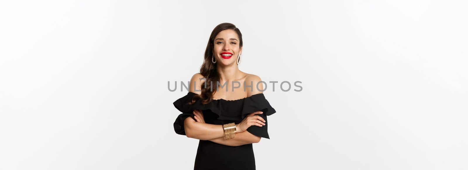 Beauty and fashion concept. Attractive female model in party dress and red lipstick, smiling pleased, looking happy, standing over white background.