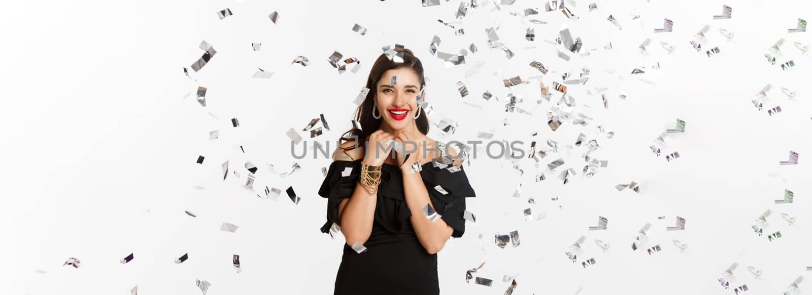 Happy woman celebrating winter holidays, smiling cheerful, partying on New Year with confetti, standing over white background.