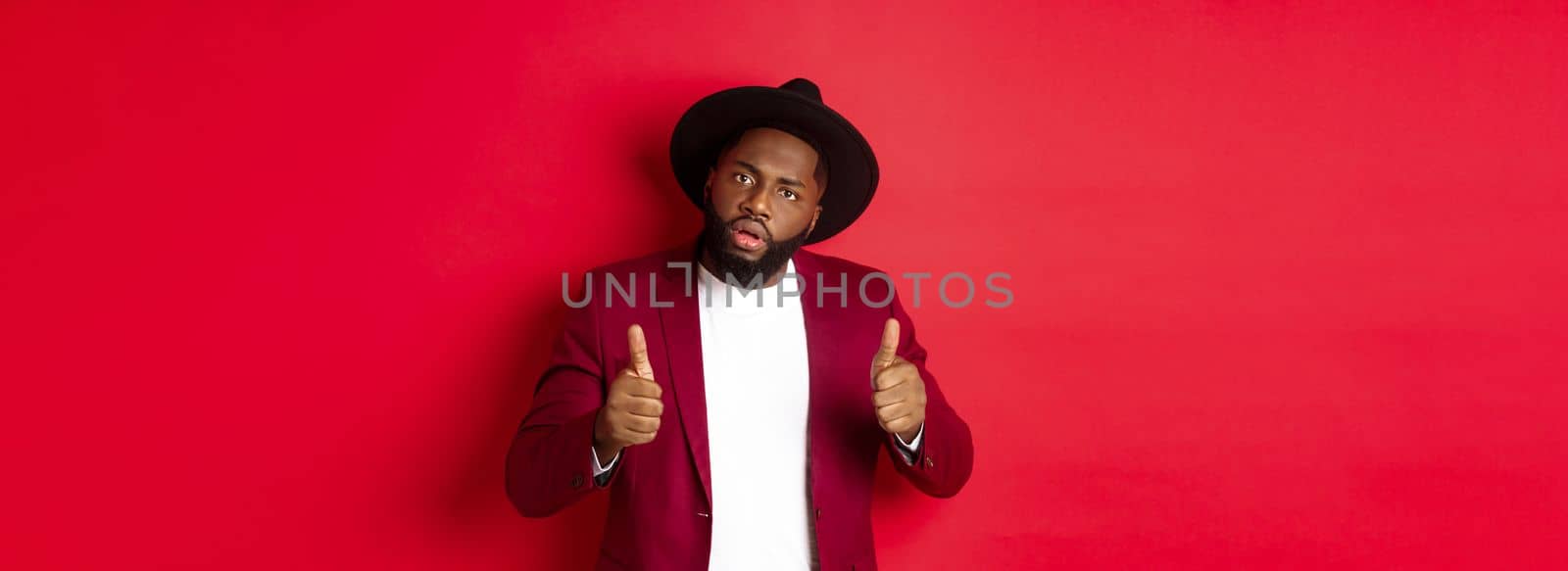 Impressed Black man saying good job, cheer up with thumbs-up, praise something, standing against red background by Benzoix