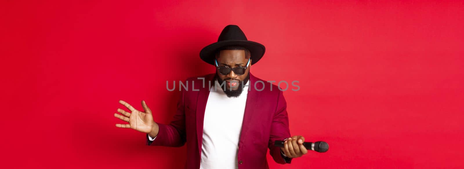 Passionate black male singer performing against red background, singing into microphone, wearing party outfit, standing over red background by Benzoix