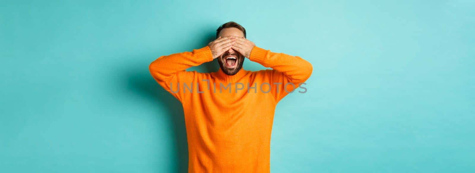 Happy bearded man waiting for surprise, shut ears and expeting gifts, standing over light blue background by Benzoix