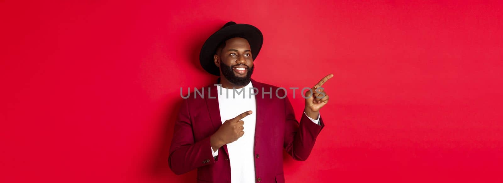 Winter holidays and shopping concept. Happy Black man pointing left and smiling, showing new year promo offer on red background.