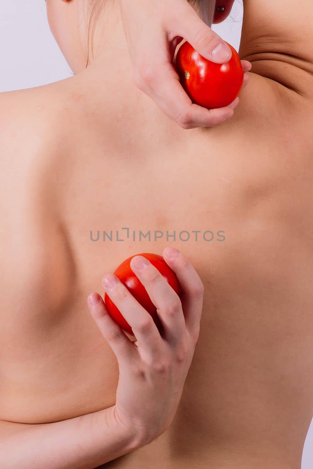 Healthy young woman holding a tomatos over her eyes, laughing, bare shoulders, topless.