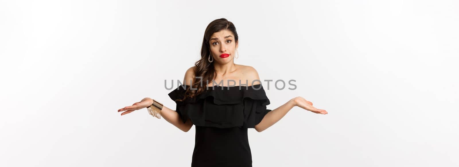 Fashion and beauty. Clueless attractive woman in black dress dont know, shrugging and smirking unaware, standing indecisive over white background.