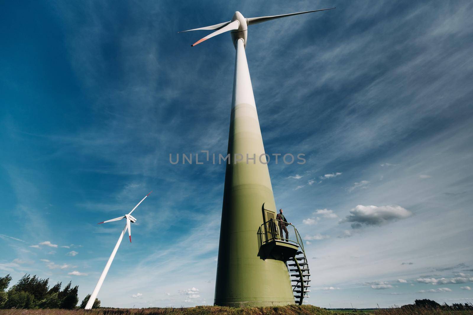 A man in a business suit with a green Golf shirt stands next to a windmill against the background of the field and the blue sky.Businessman near the windmills.Modern concept of the future