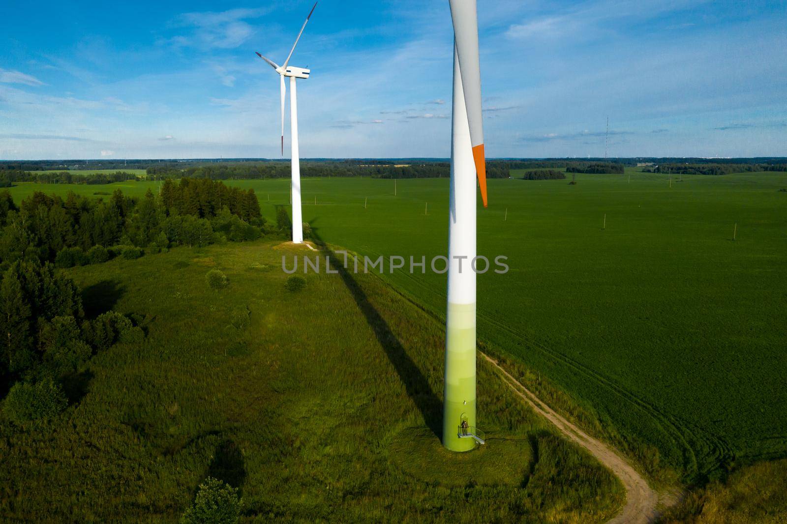 A man in a business suit with a green Golf shirt stands next to a windmill against the background of the field and the blue sky.Businessman near the windmills.Modern concept of the future