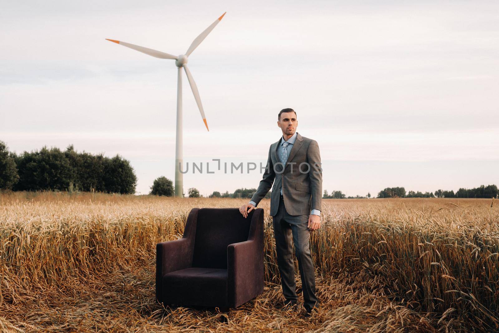 Portrait of a businessman in a gray suit and tie, standing near a chair in a wheat field.Europe.