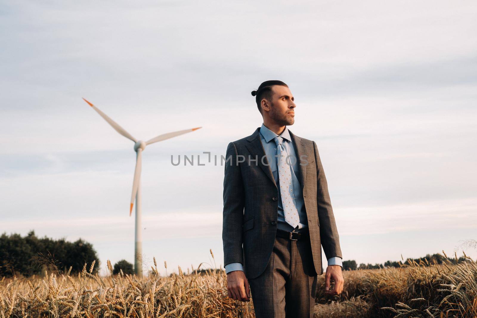 Portrait of a businessman in a gray suit on a wheat field against the background of a windmill and the evening sky by Lobachad