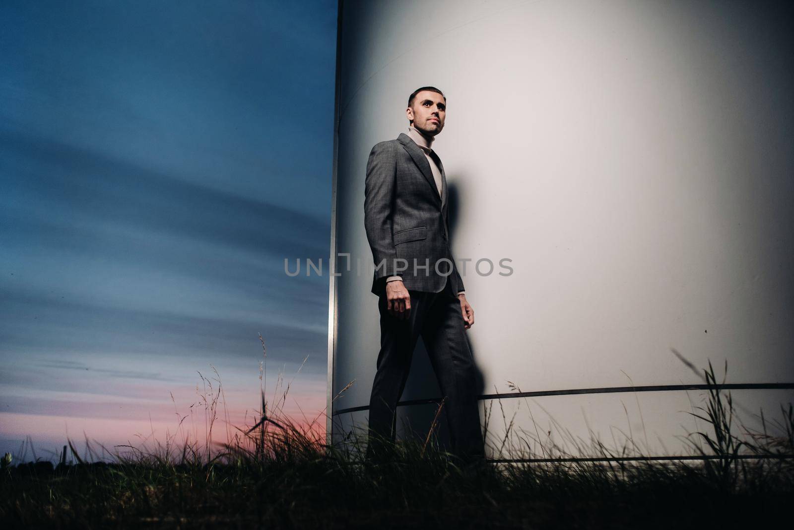 A man in a grey business suit stands next to a windmill after sunset .Businessman near windmills at night.Modern concept of the future