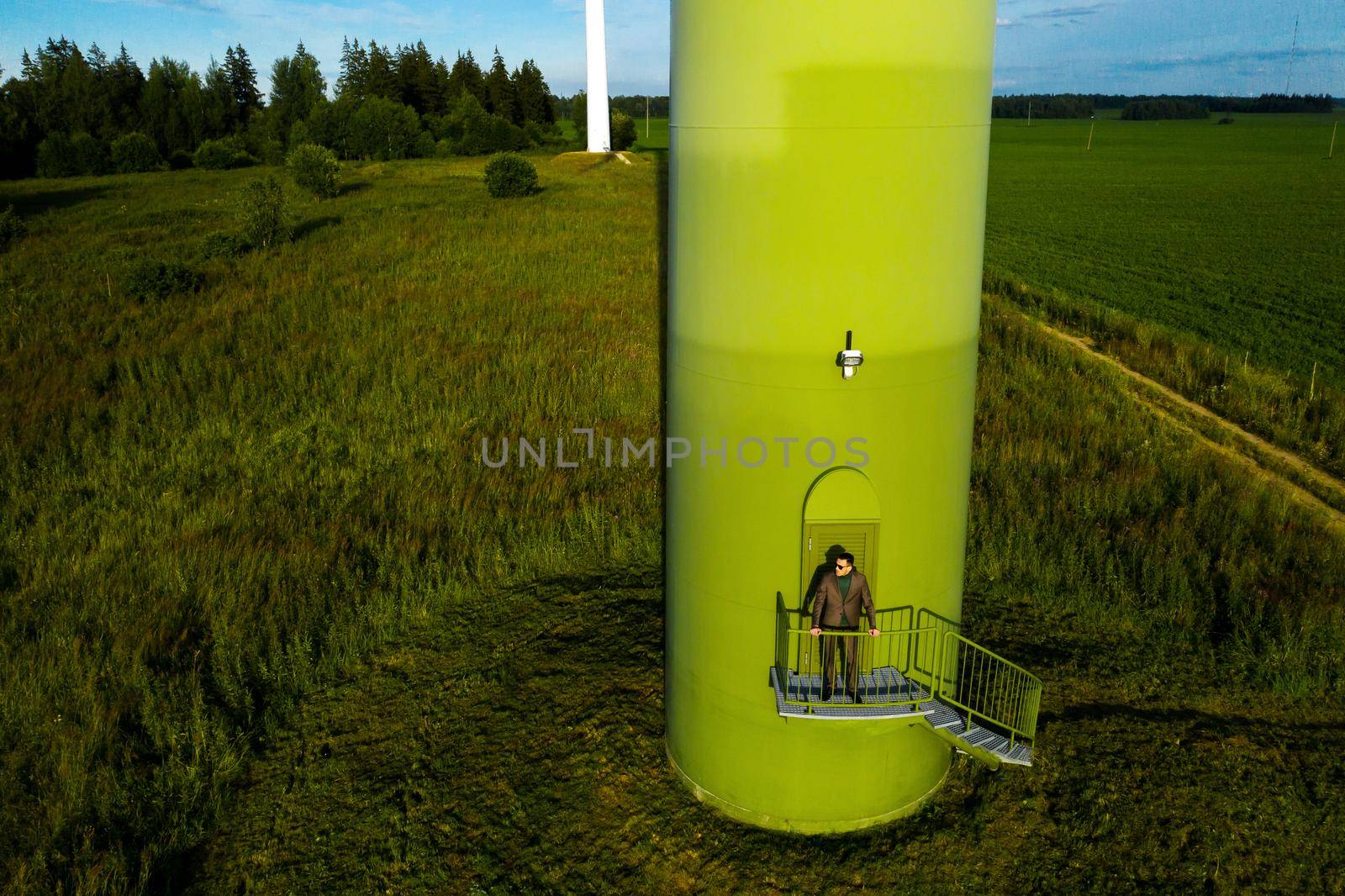 A man in a business suit with a green Golf shirt stands next to a windmill against the background of the field and the blue sky.Businessman near the windmills.Modern concept of the future