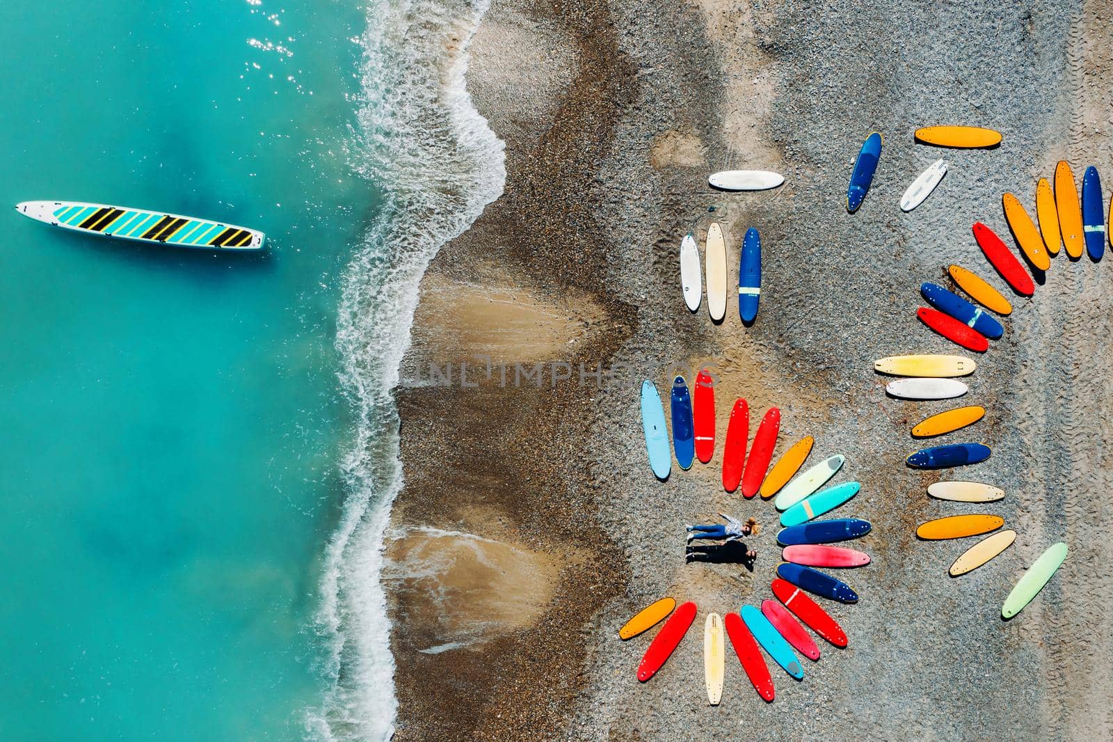 a beautiful couple is lying on the beach of France next to surfboards, shooting from a quadcopter, a lot of surfboards are unusually lying on the beach.