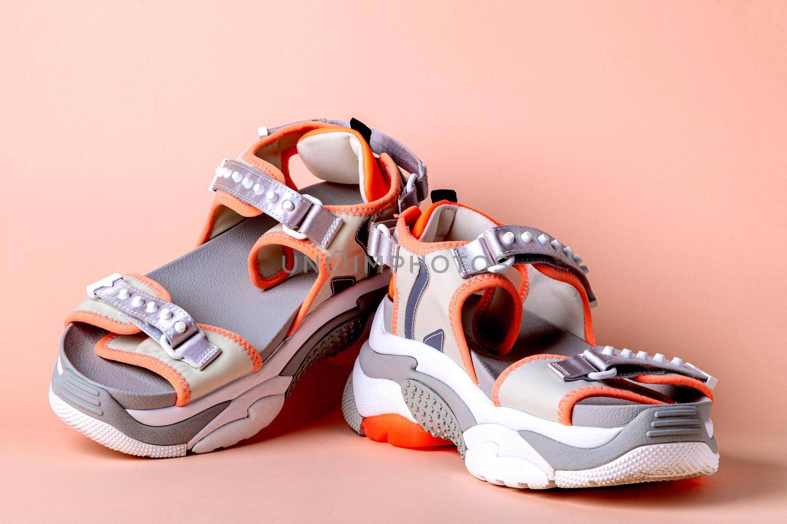 Women's, fashionable, sports sandals with orange accents on a pink background. New youth shoes for girls. Front view.