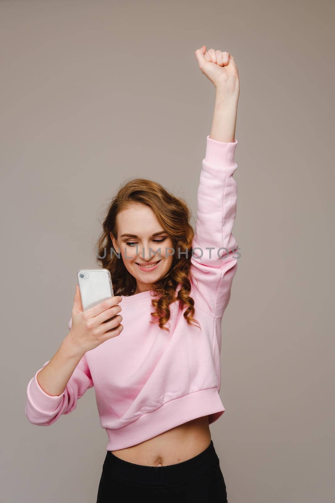 A happy young girl holds the phone looks into it and smiles holding her hand up by Lobachad