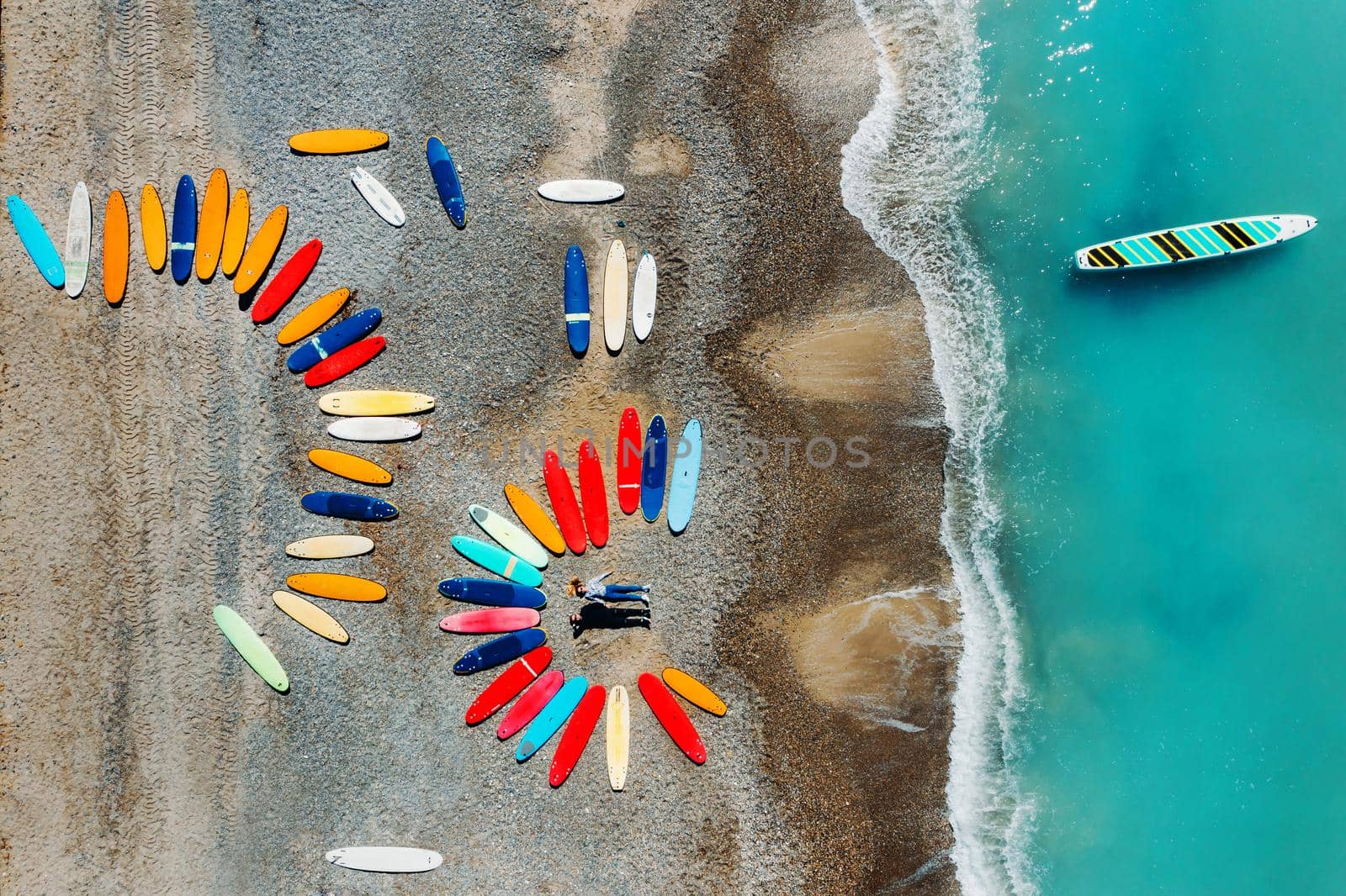 a beautiful couple is lying on the beach of France next to surfboards, shooting from a quadcopter, a lot of surfboards are unusually lying on the beach by Lobachad