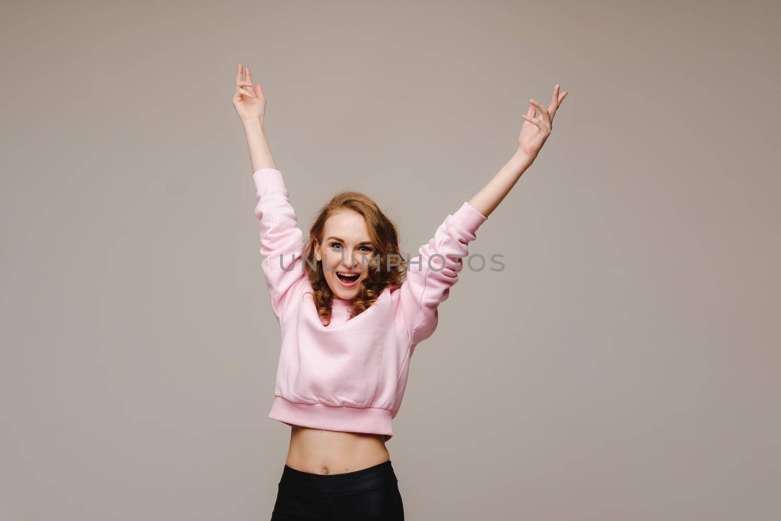 A beautiful emotional girl raises her hands up from happiness and what she sees on a gray background.