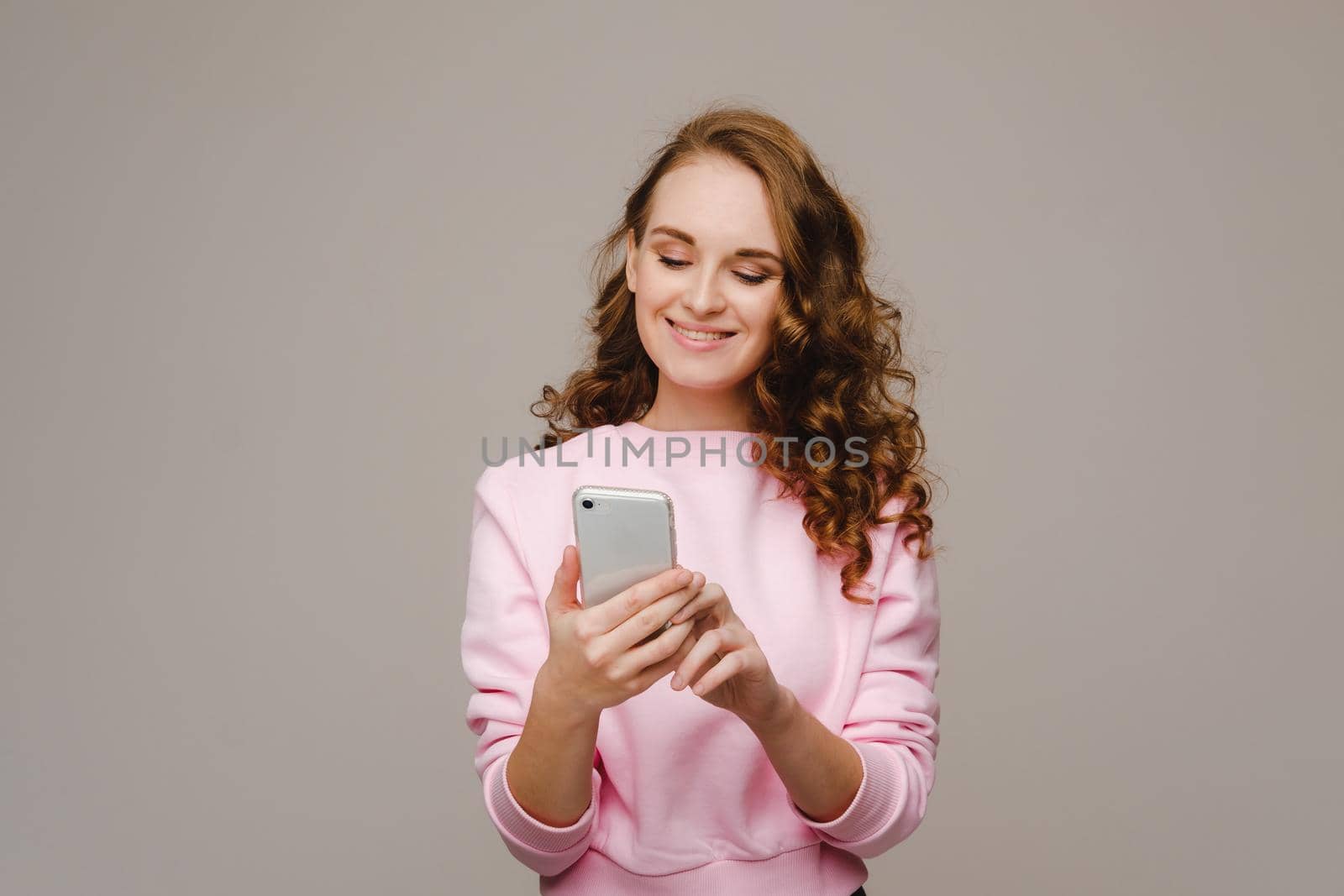 A happy young girl holding a phone looks into it and smiles by Lobachad