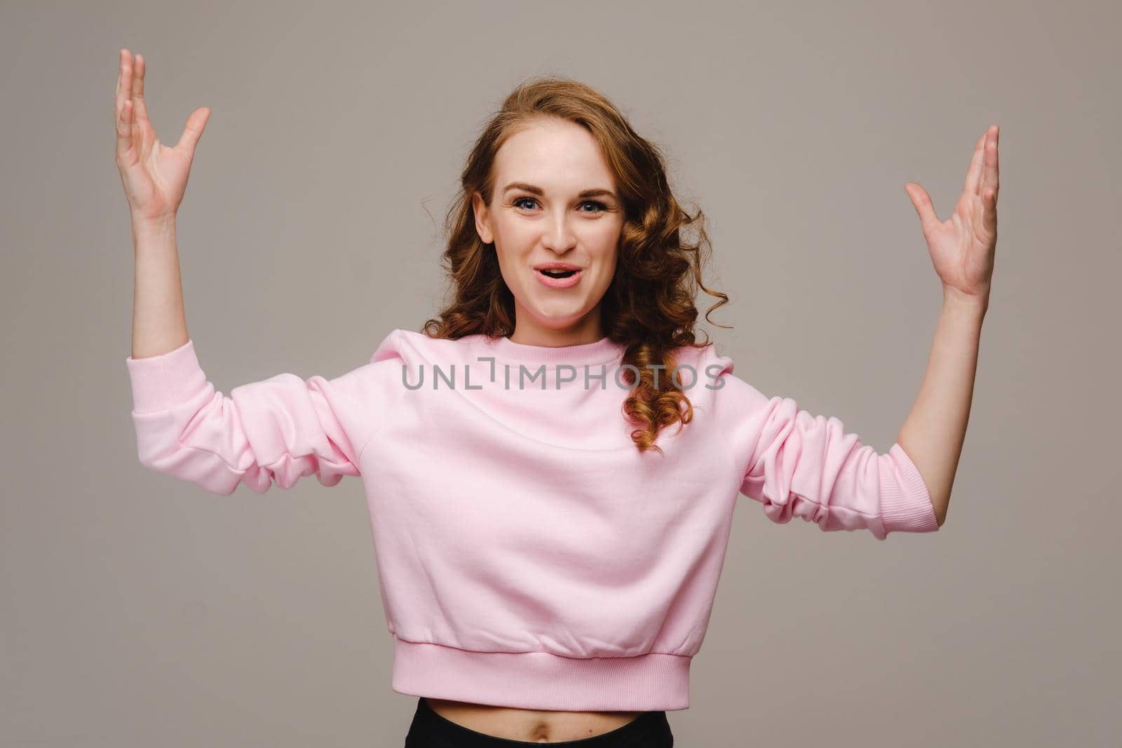 A beautiful girl on a gray background holds her head and screams emotionally.