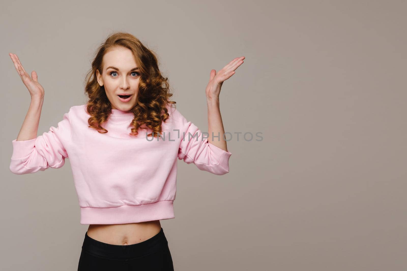 A beautiful emotional girl raises her hands up from happiness and what she sees on a gray background.