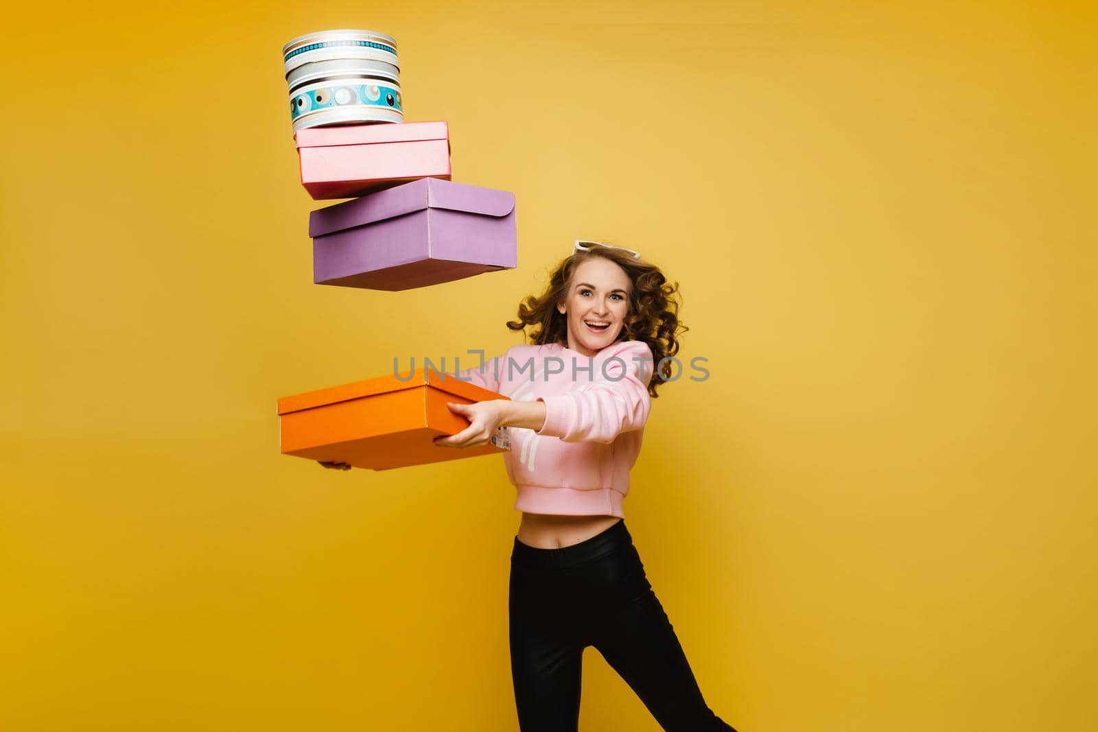 A happy young woman with colorful paper boxes after shopping isolated on an orange Studio background. Seasonal sales, purchases, spending money on gifts.