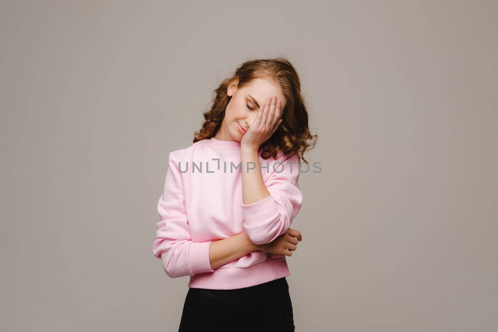 a girl with long hair on a gray background suffering from a headache holds her head with her hands. The girl puts her hands on her head, isolated against a gray background. The concept of problems and headaches
