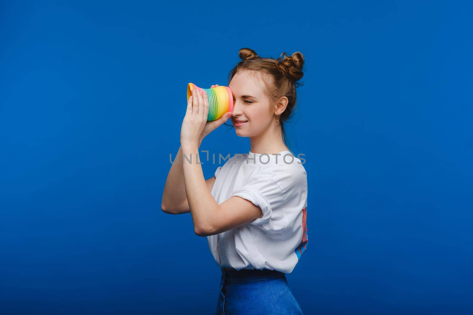 Beautiful young girl playing with a rainbow slinky, a toy of her childhood on a blue background.