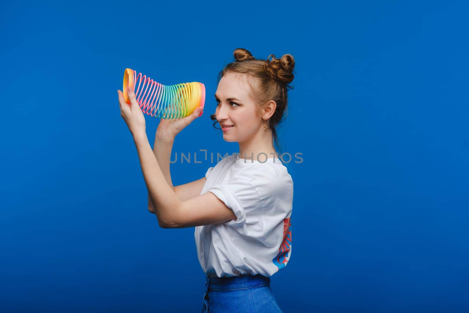 Beautiful young girl playing with a rainbow slinky, a toy of her childhood on a blue background.