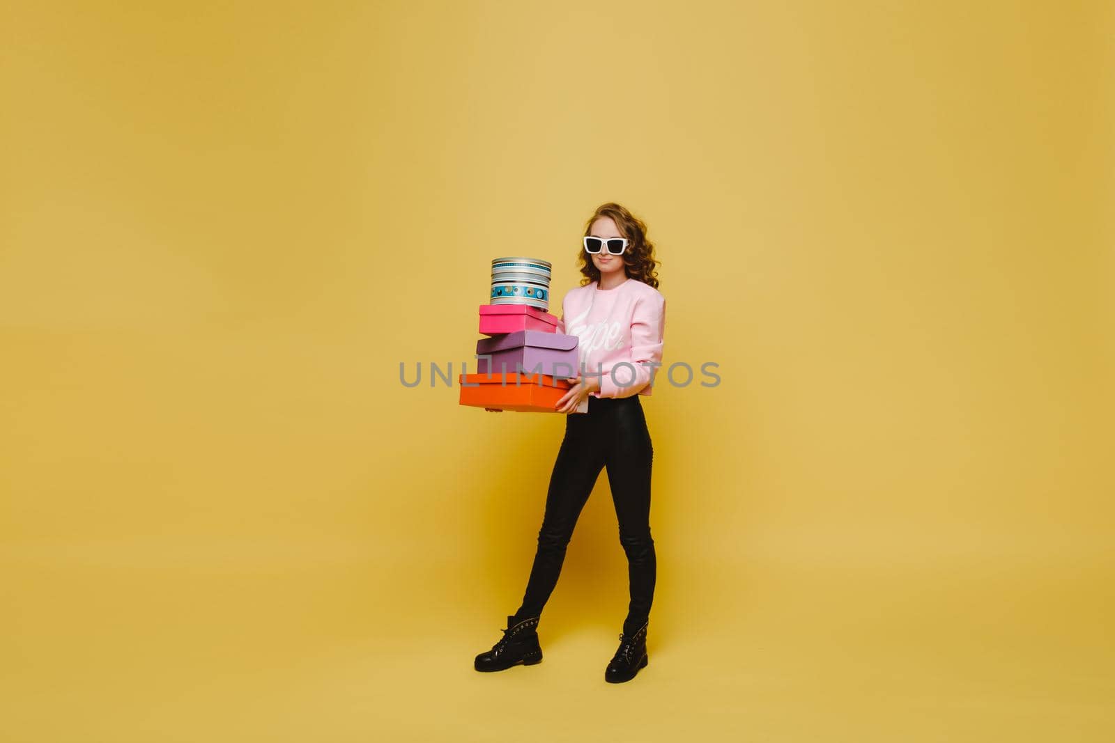 A happy young woman with colorful paper boxes after shopping isolated on an orange Studio background. Seasonal sales, purchases, spending money on gifts.