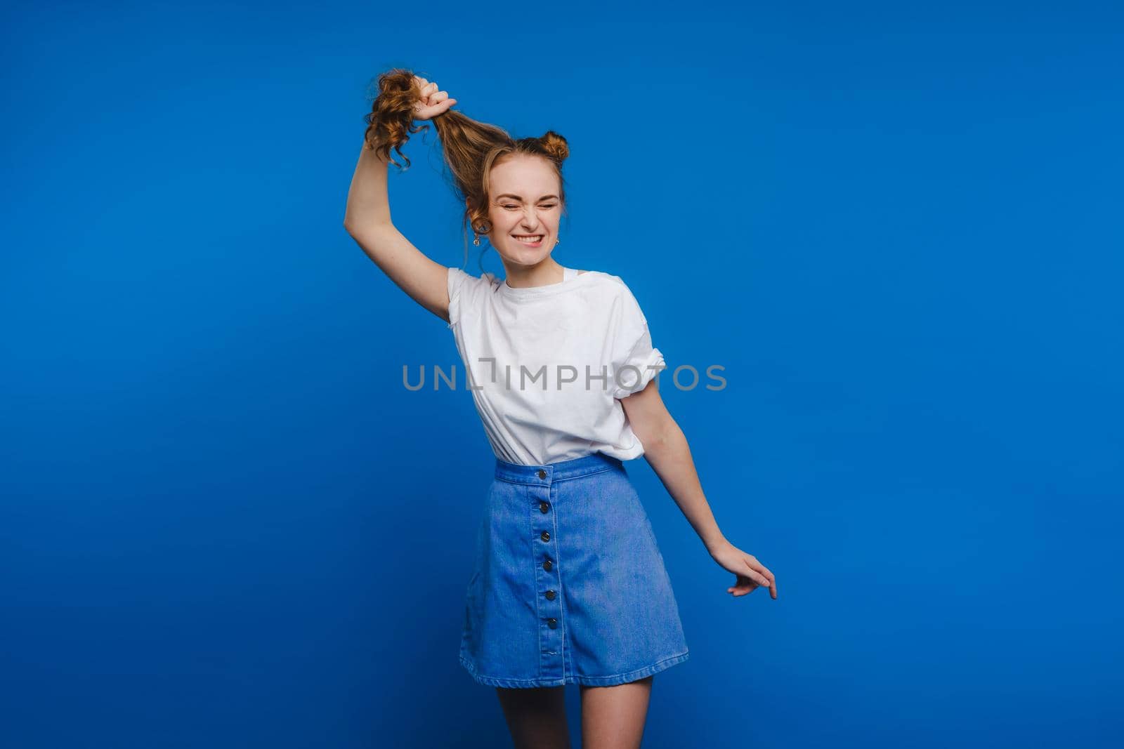 A young stylish girl pulls her hair on a blue background, a Model pulls her long hair