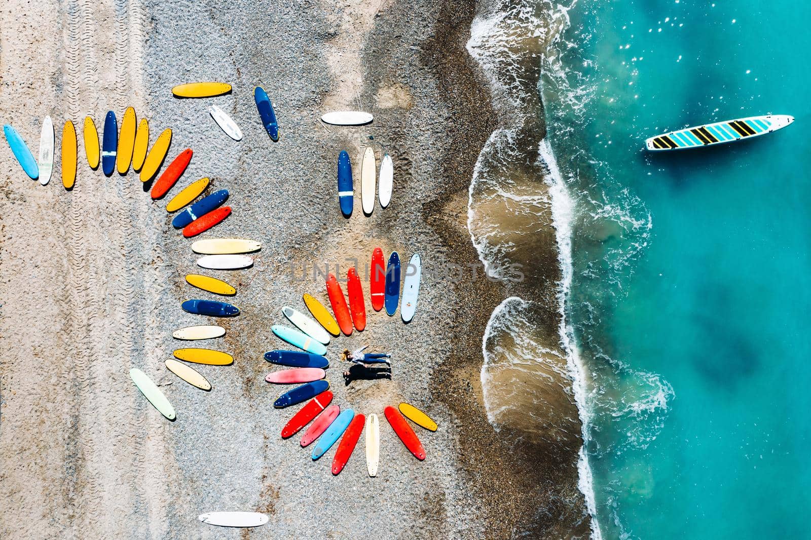 a beautiful couple is lying on the beach of France next to surfboards, shooting from a quadcopter, a lot of surfboards are unusually lying on the beach by Lobachad