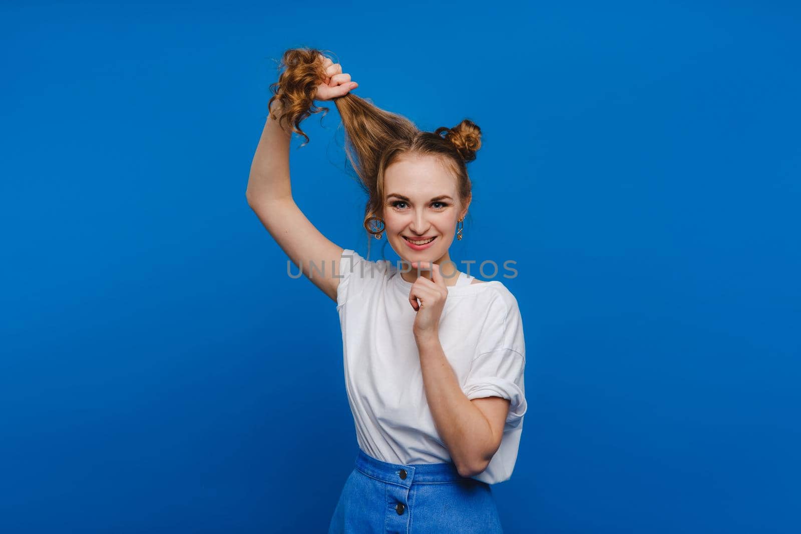 A young stylish girl pulls her hair on a blue background, a Model pulls her long hair