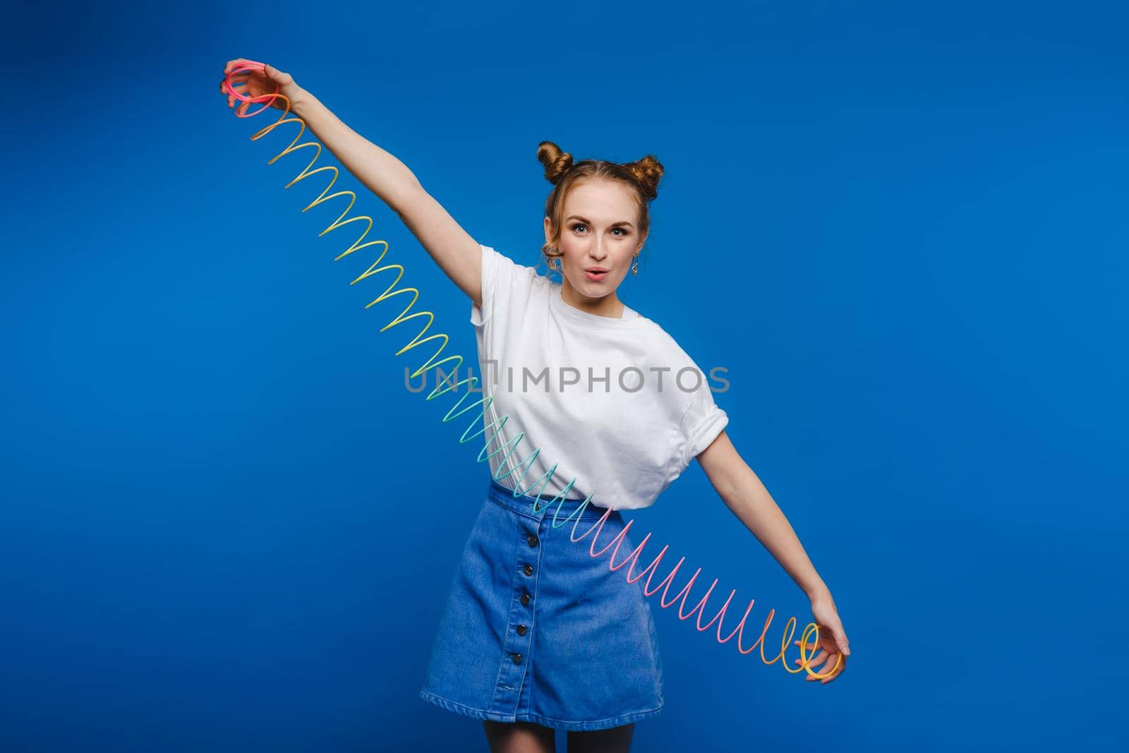 Beautiful young girl playing with a rainbow slinky, a toy of her childhood on a blue background.