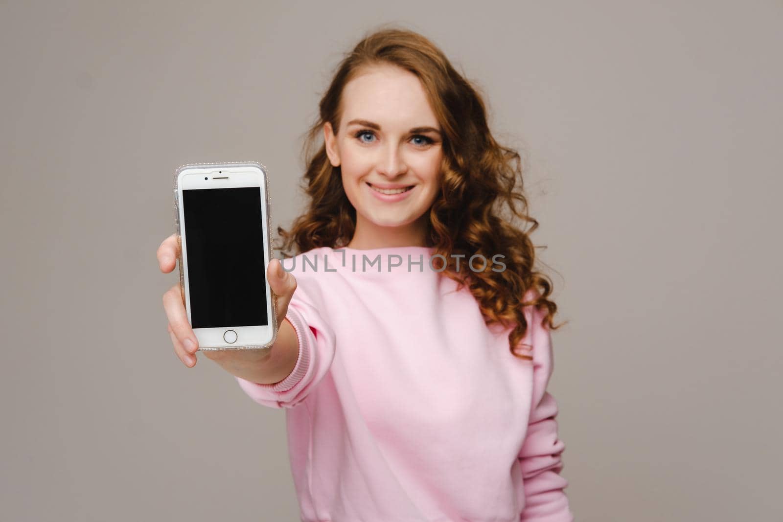 Fashionable girl with a smartphone on the background. Stands and shows the smartphone.