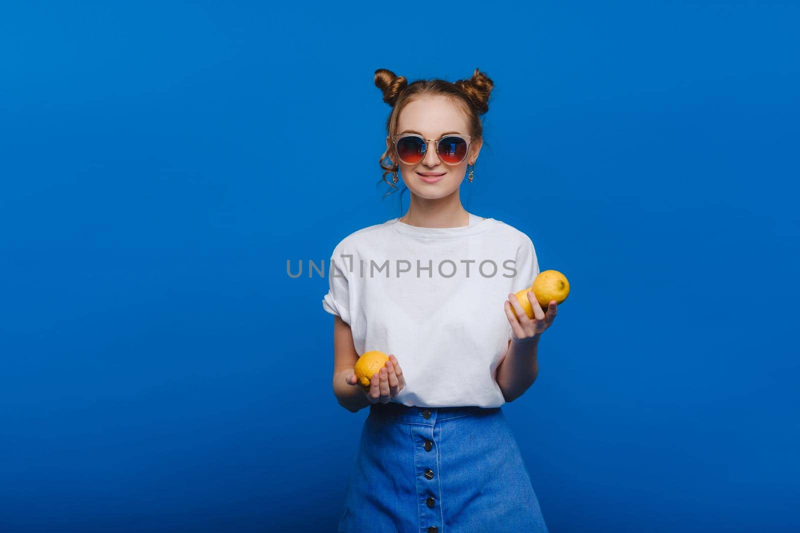 a young beautiful girl standing on a blue background holding lemons in her hand. Smiles.
