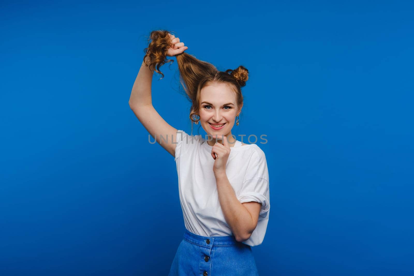 A young stylish girl pulls her hair on a blue background, a Model pulls her long hair