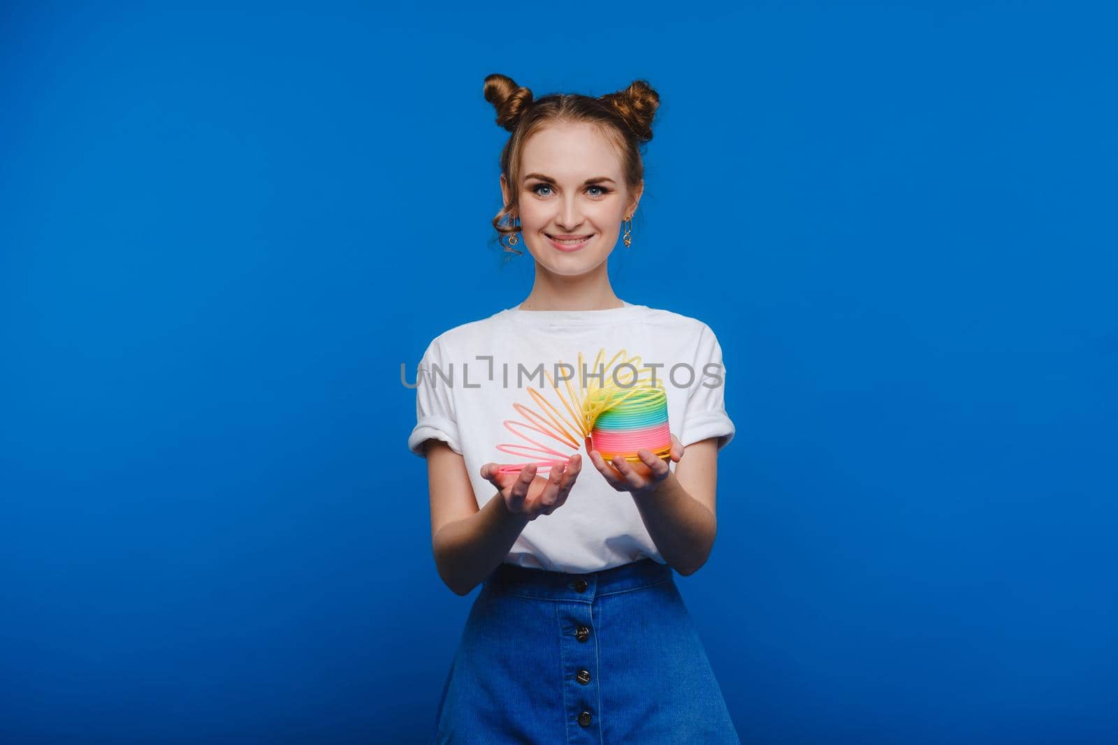 Beautiful young girl playing with a rainbow slinky, a toy of her childhood on a blue background.