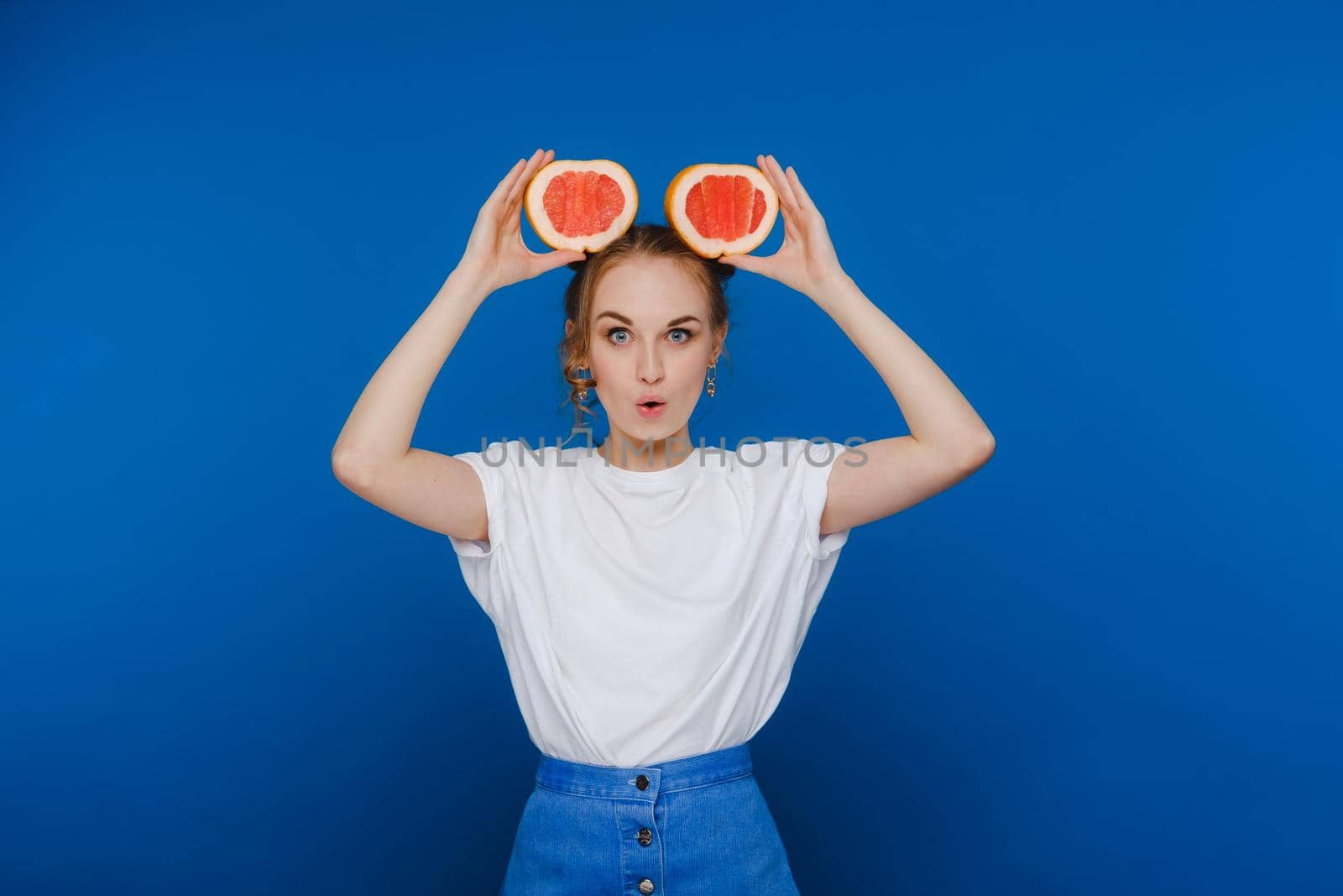Surprised, the laughing girl holds the grapefruit like ears. Vegan lifestyle. Smiling woman , eating concept.Diet organic , weight loss and healthy food. Smoothies and fresh juice