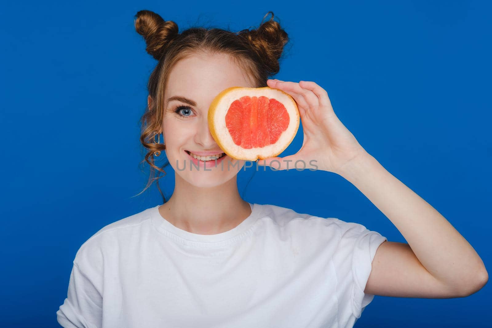 Surprised, the laughing girl holds the grapefruit like ears. Vegan lifestyle. Smiling woman , eating concept.Diet organic , weight loss and healthy food. Smoothies and fresh juice
