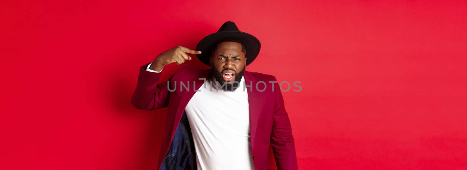Angry Black man scolding person for being stupid, pointing at head and looking pissed-off, standing against red background by Benzoix