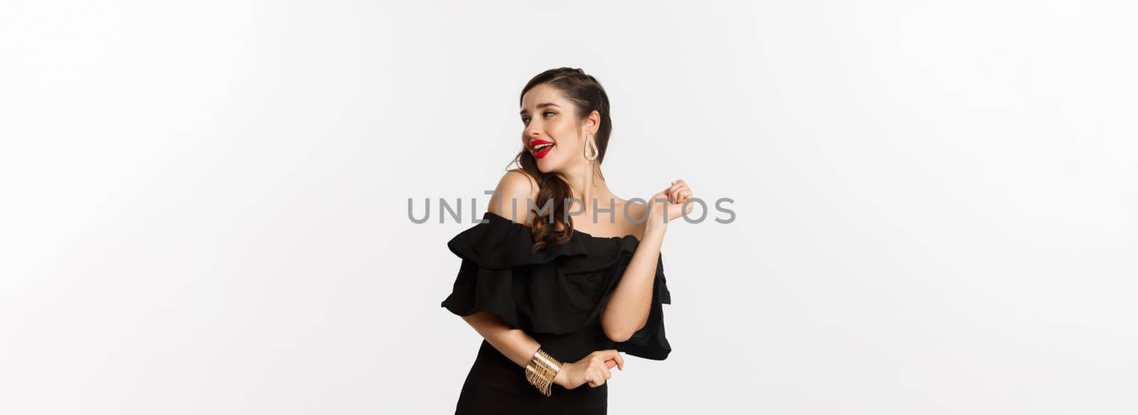 Fashion and beauty. Woman celebrating and dancing in black dress, having fun and smiling, standing over white background.