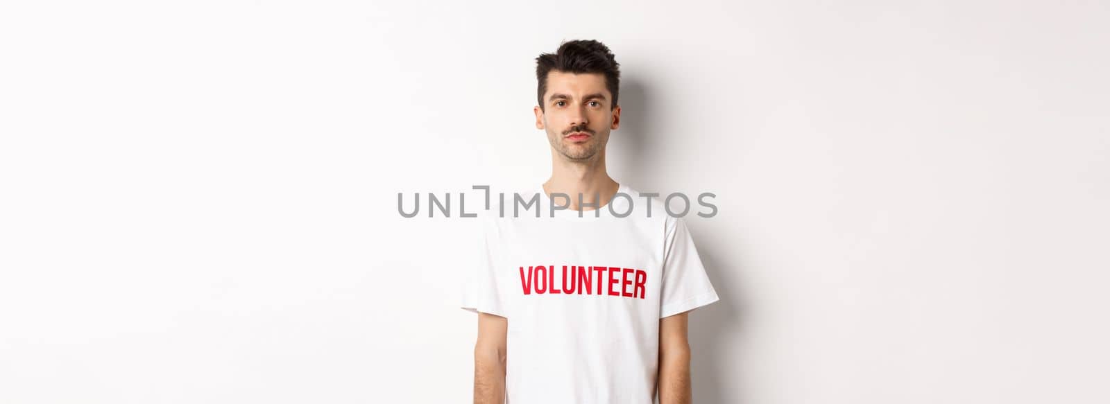 Serious young male volunteer in white t-shirt looking at camera, ready to help.