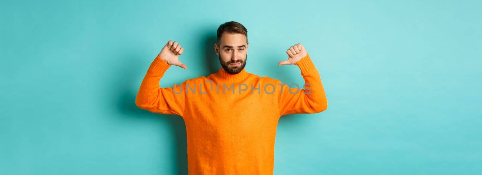 Confident attractive guy pointing at himself, show-off or brag, standing over light blue background.
