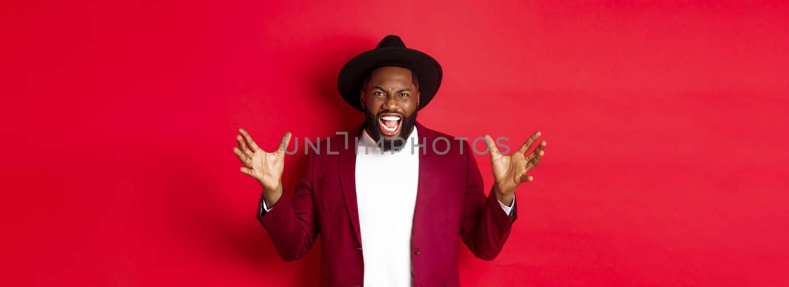 Angry Black man screaming and shaking hands with hatred, losing temper, standing outraged against red background by Benzoix
