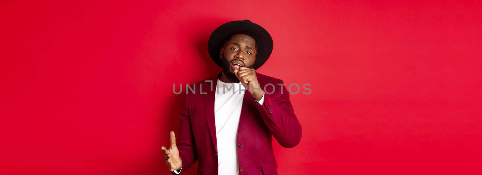Christmas shopping and people concept. Handsome Black male model in party outfit singing in invisible microphone, looking passionate at camera, red background.