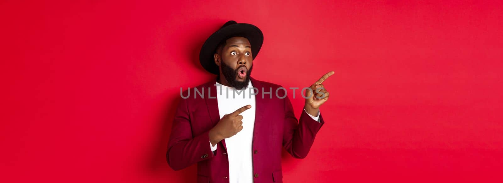 Winter holidays and shopping concept. Happy Black man pointing left and smiling, showing new year promo offer on red background.